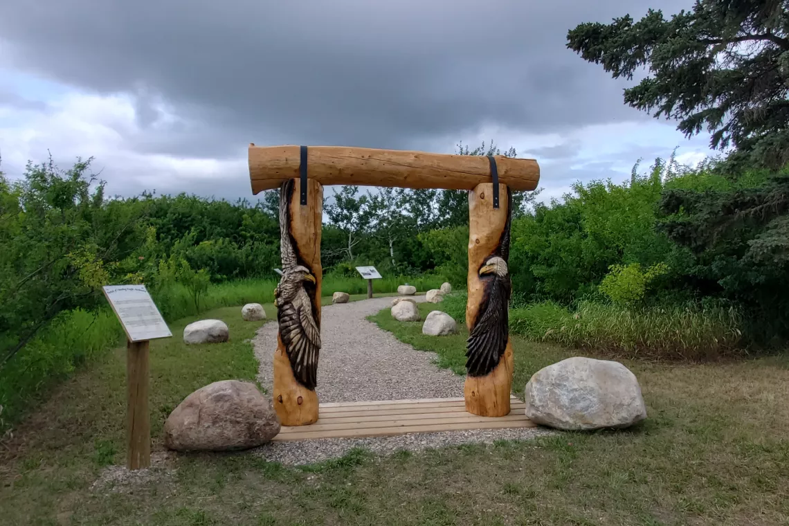 Forested outdoor space with a wooden sculpture shaped as a portal depicting two birds of prey.