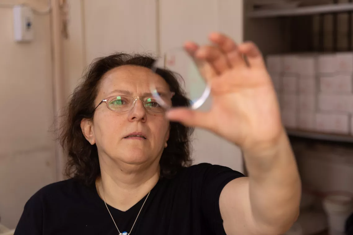 A woman is examining a transparent object held up to the light, focusing intently on it. She's indoors, with shelves in the background.