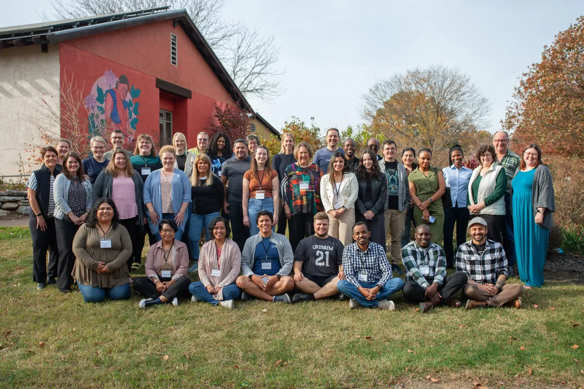 A diverse group of about 40 people stand in rows and sit on the grass.