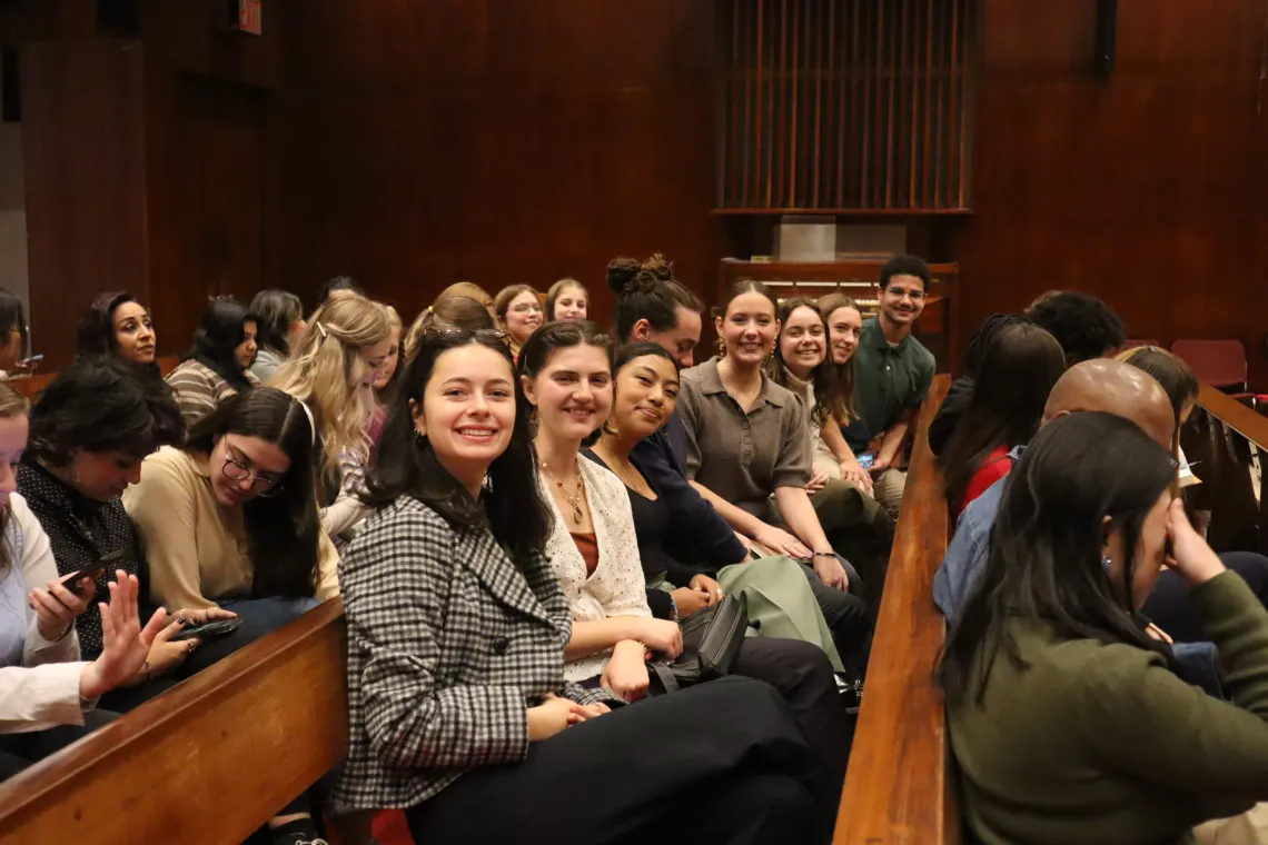 Students are sat in a row and smile at the camera. 