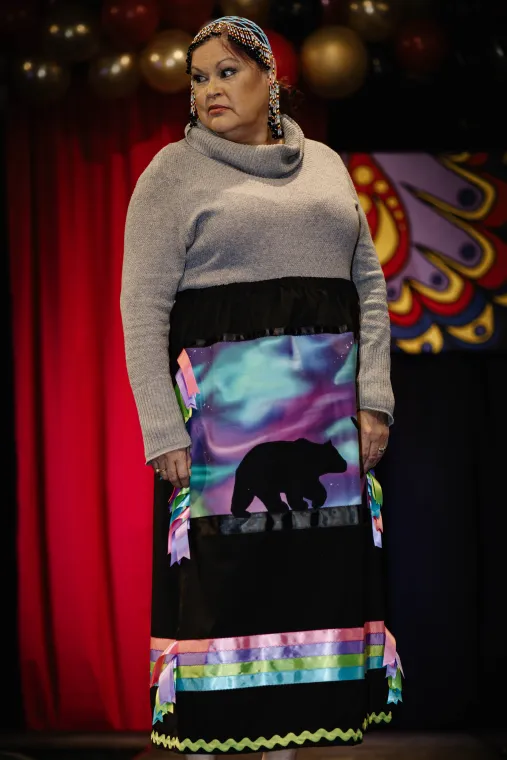 A woman models a vibrant Indigenous designed skirt featuring a polar bear against northern lights.