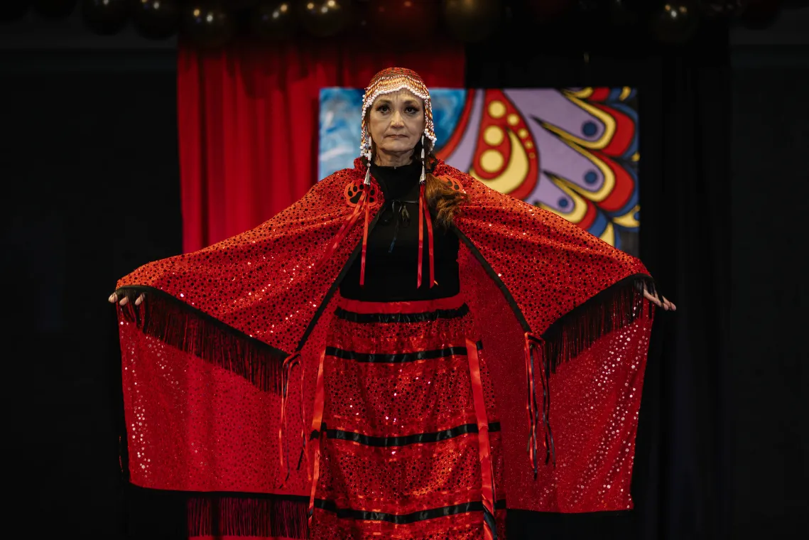 A woman models a vibrant red Indigenous designed outfit.