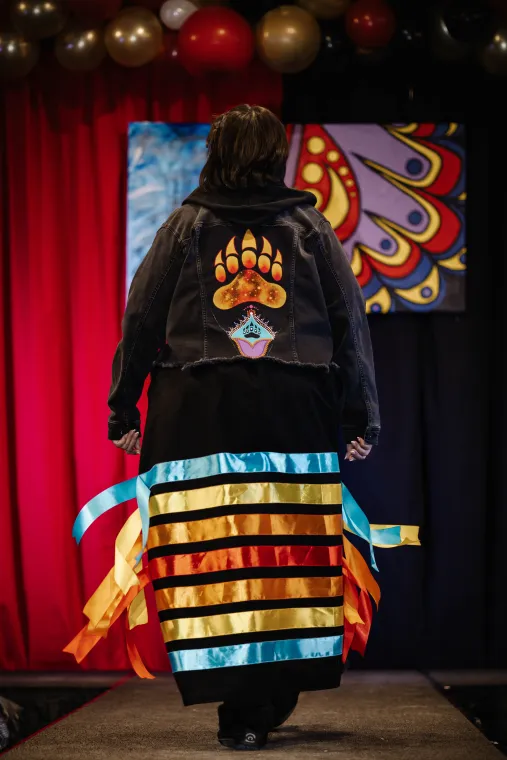 A woman models the back of an Indigenous designed outfit showing a bear paw