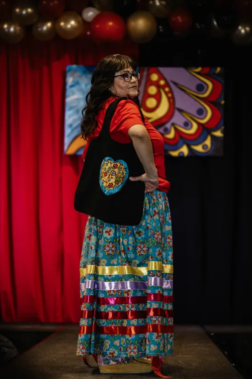 A woman models a vibrant Indigenous designed outfit.