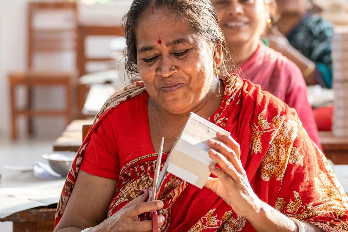 A smiling woman with scissors cuts a paper product she is holding.
