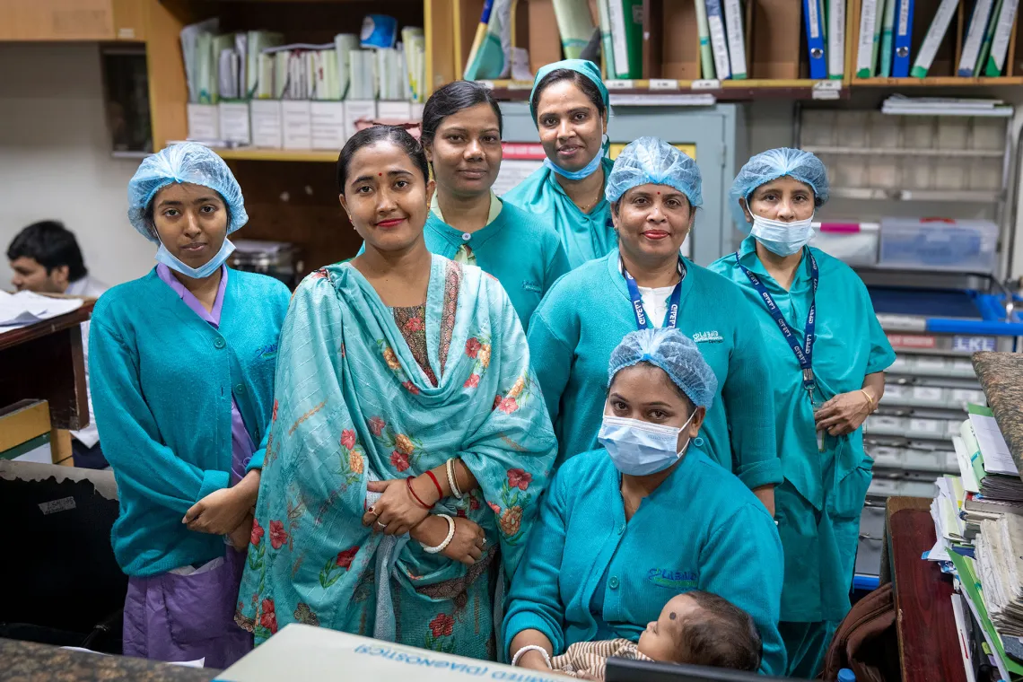 Seven people in hospital scrubs smile at the camera. One is wearing a sari.