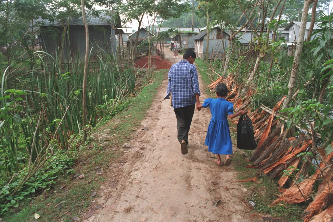 An older sibling holds a younger sibling's hand as they walk down a path.