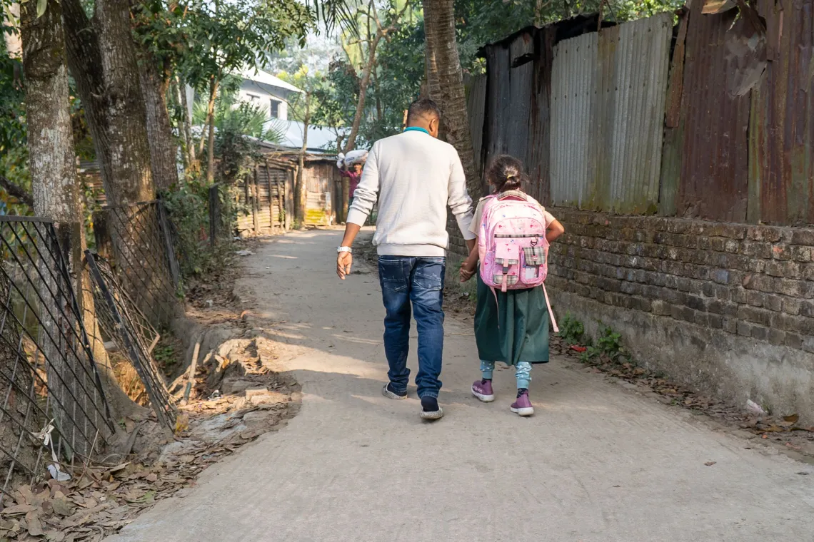 A parent holds their kid's hand as they walk down a narrow street.