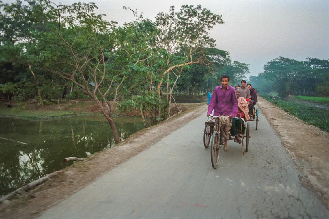 A man pedals a 3-wheeled cart down a narrow road.