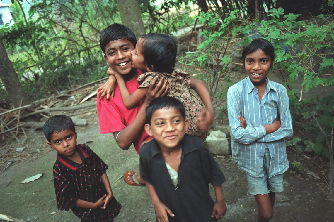 A smiling older child receives a smooch from a younger child while three other kids smile at the camera.