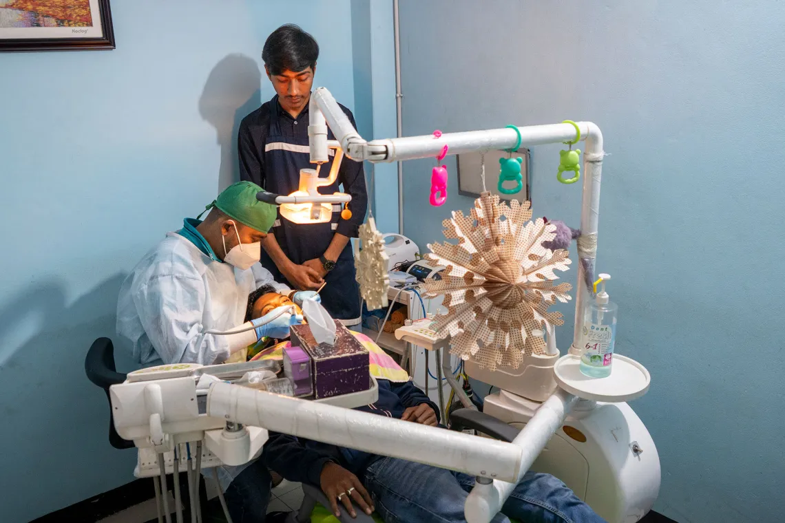 A dentist in scrubs is working on a patients mouth while their assistant observes.