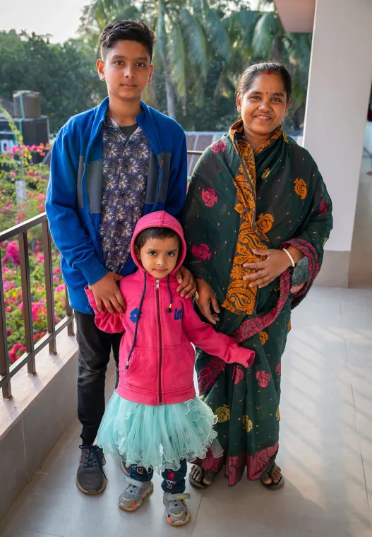 A woman stands with her two children. The older one is taller than her and the younger is much shorter.