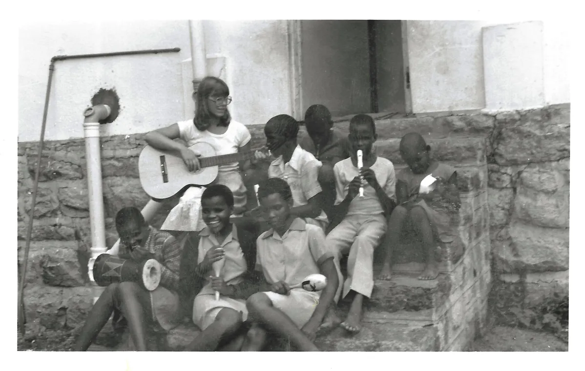 Lady playing a guitar to a group of kids.