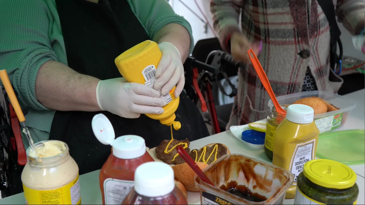 A pair of hands adds condiments to a burger at the weekly barbecue ran by MCC BC's Homelessness Outreach and Prevention program