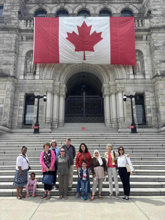 A group standing on the steps of the BC Parliament building, with the Canadian flag overhead.