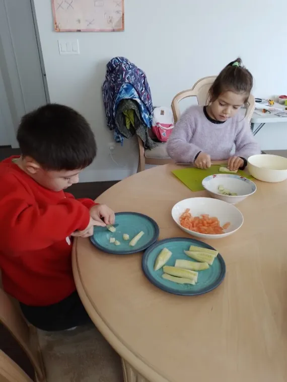 Two children slice vegetables at a table