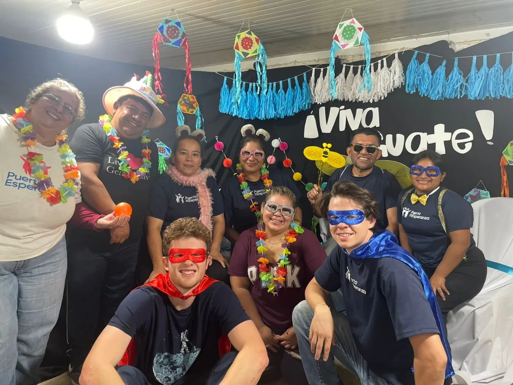 A group of people wearing costumes and accessories, posing together in a decorated space with festive decorations and a cheerful atmosphere.