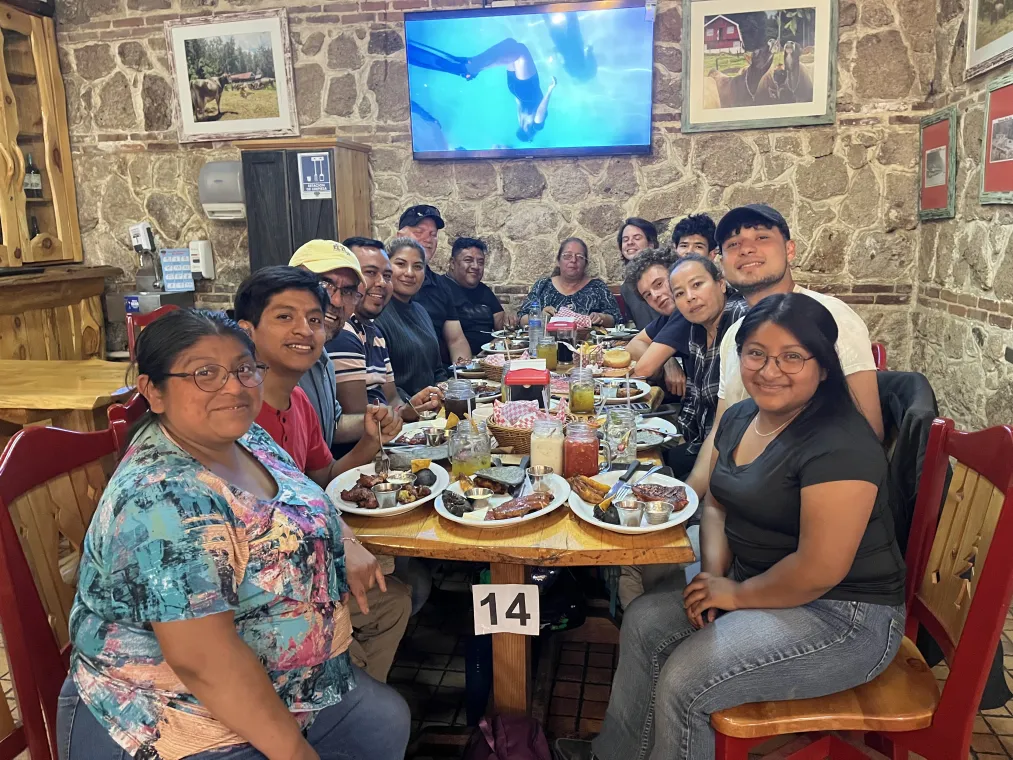 A group of people gathered around a table filled with food, smiling and enjoying a meal in a restaurant setting.