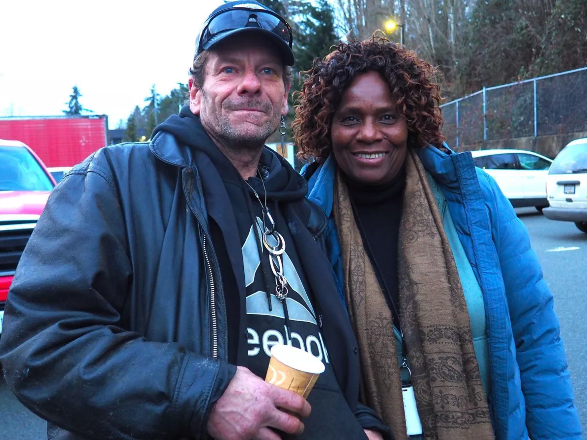 Two people standing side by side, one is holding a paper cup and the other is wearing a food glove.