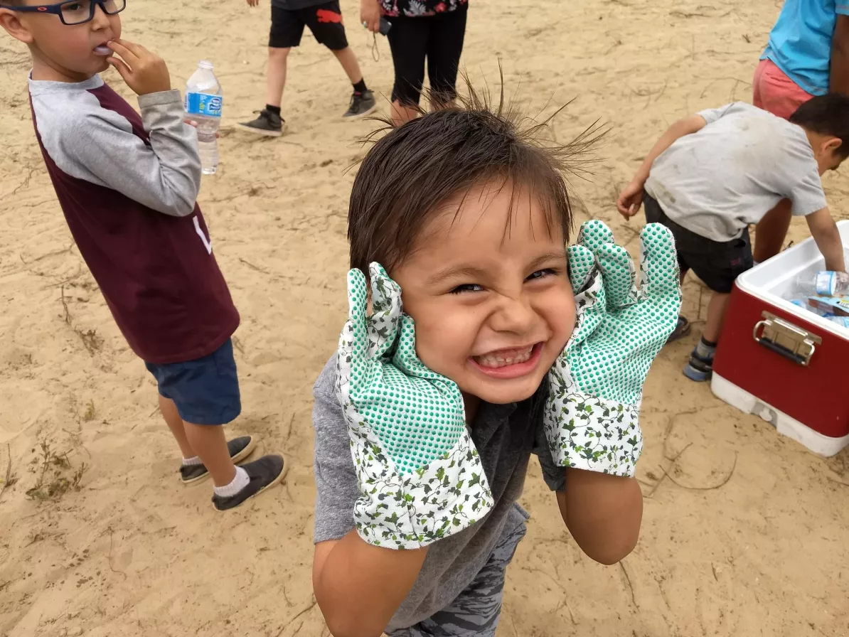 A child with large gardening gloves cups their face with their hands