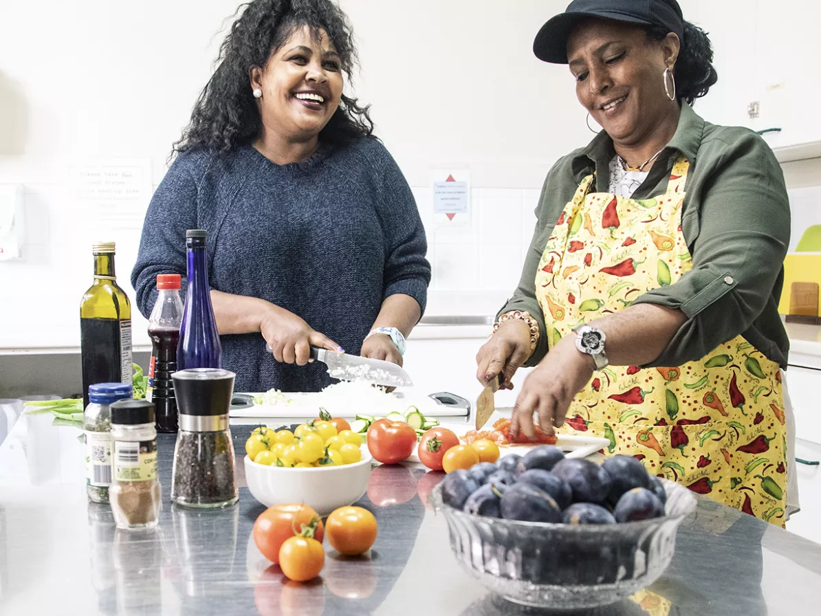 Two women in a kitchen work at cutting vegetables.