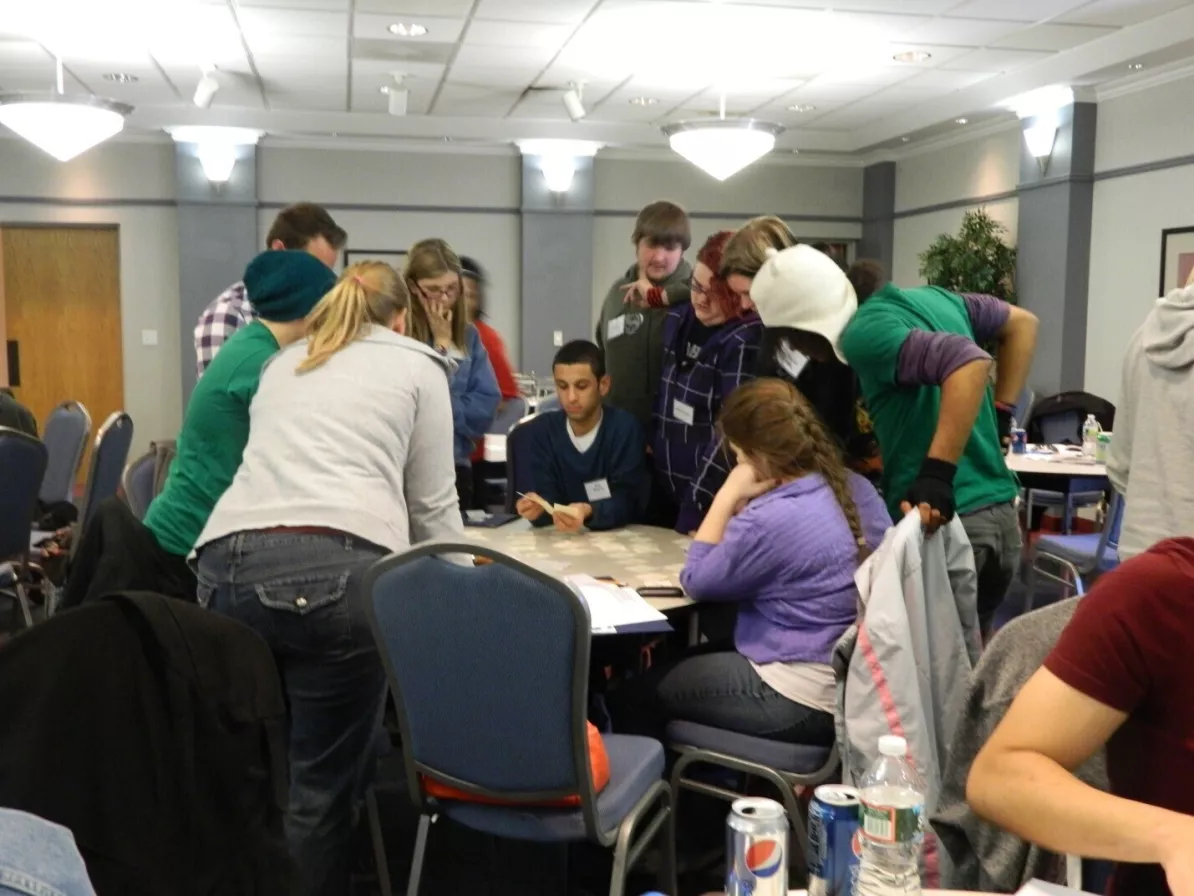 A group of young adults sit and stand around a table