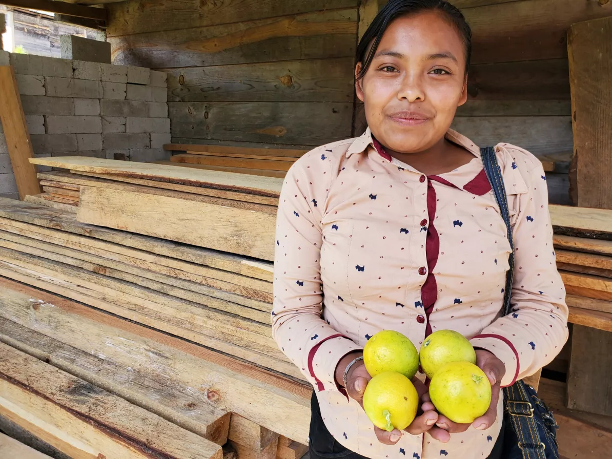 A Mexican woman holds four yellow fruit in her hands