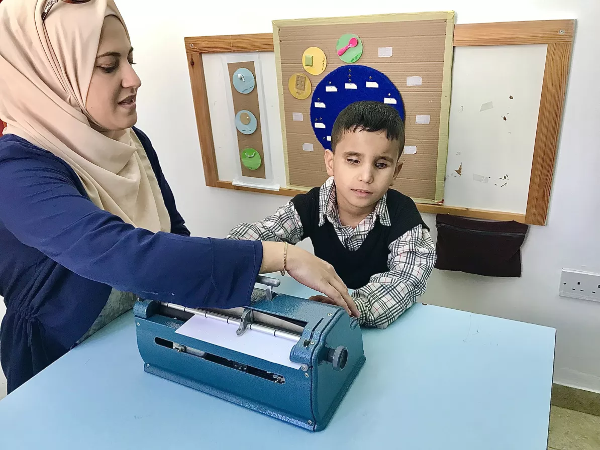 A woman helps a child write on a Braille machine