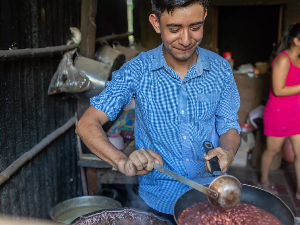 A Salvadoran man in a blue shirt ladles beans