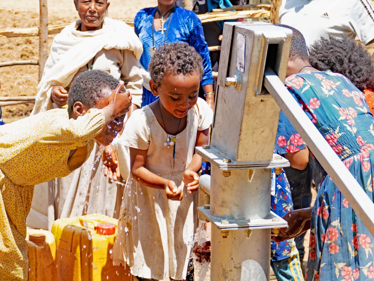 Ethiopian children at a well. One child is splashing water on their face.