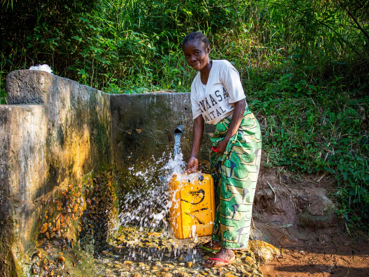 Germaine Kambundi, 46, draws water from a spring which she used before the borehole was drilled in her village.