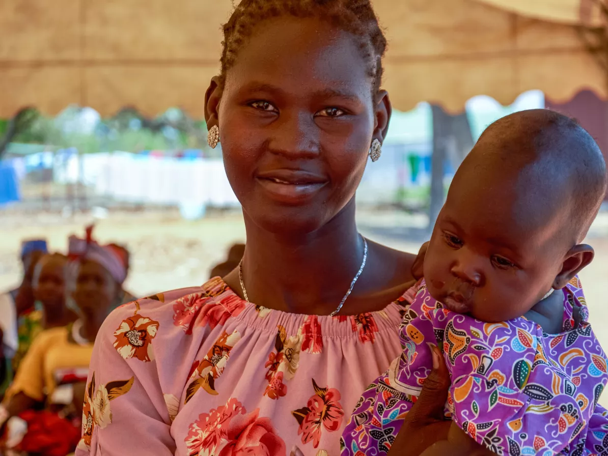 A woman holds a child and smiles at the camera