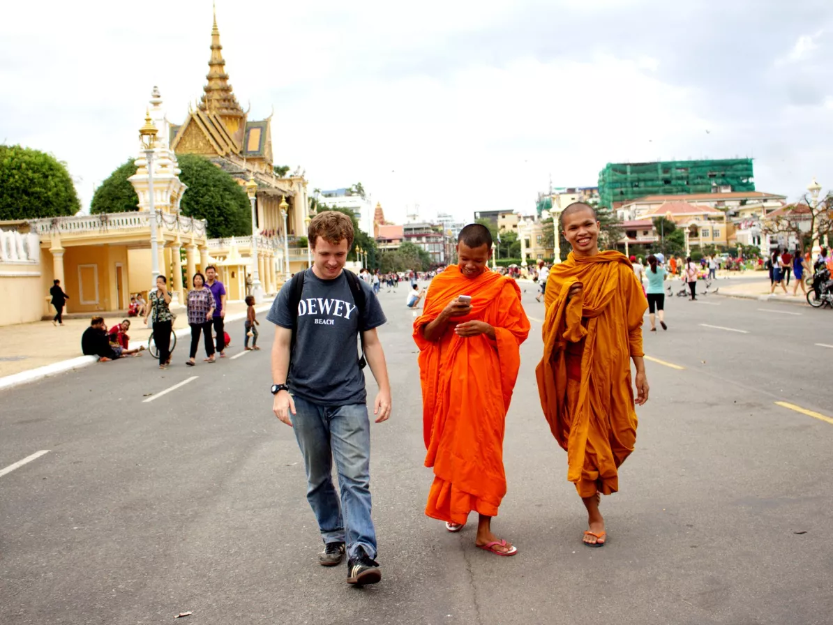 A young man and two Buddhist monks in orange robes walk down a road in Cambodia