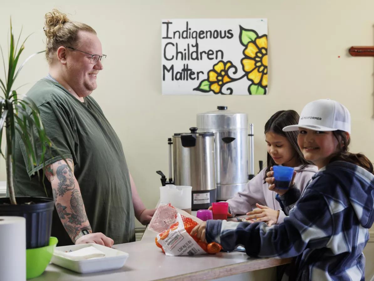 A person behind a counter serves drinks to two young girls who are helping themselves to oranges