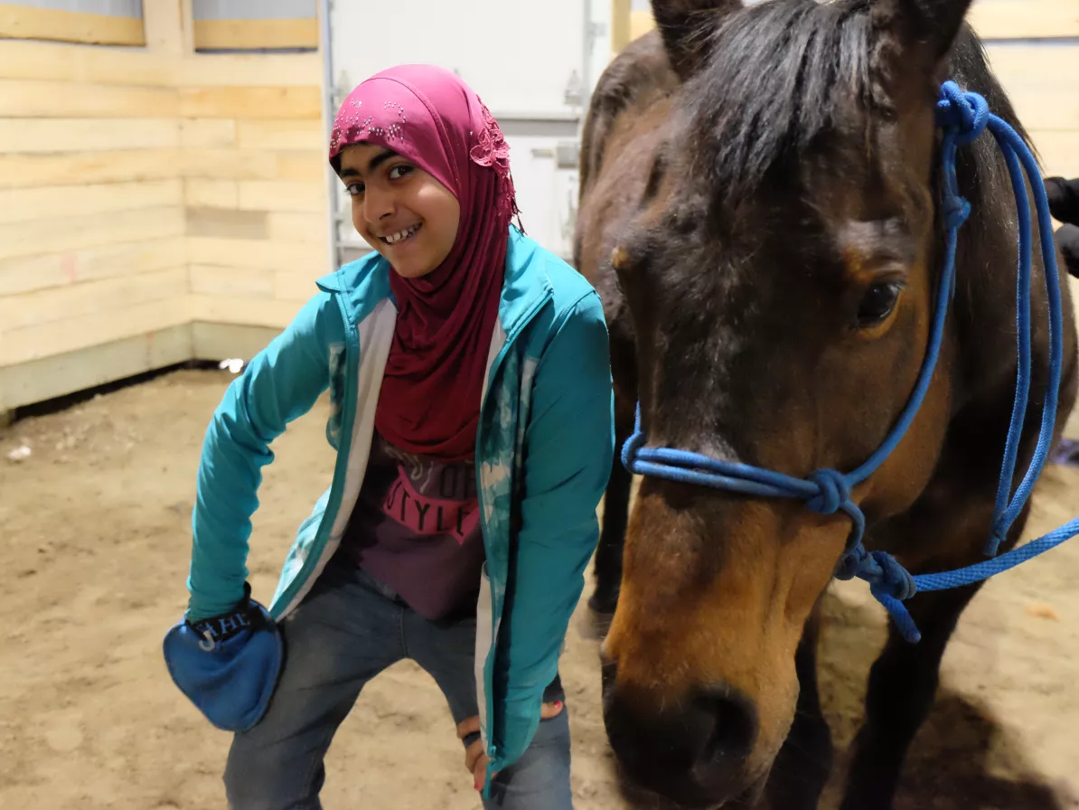 A girl in a purple hijab poses with a horse