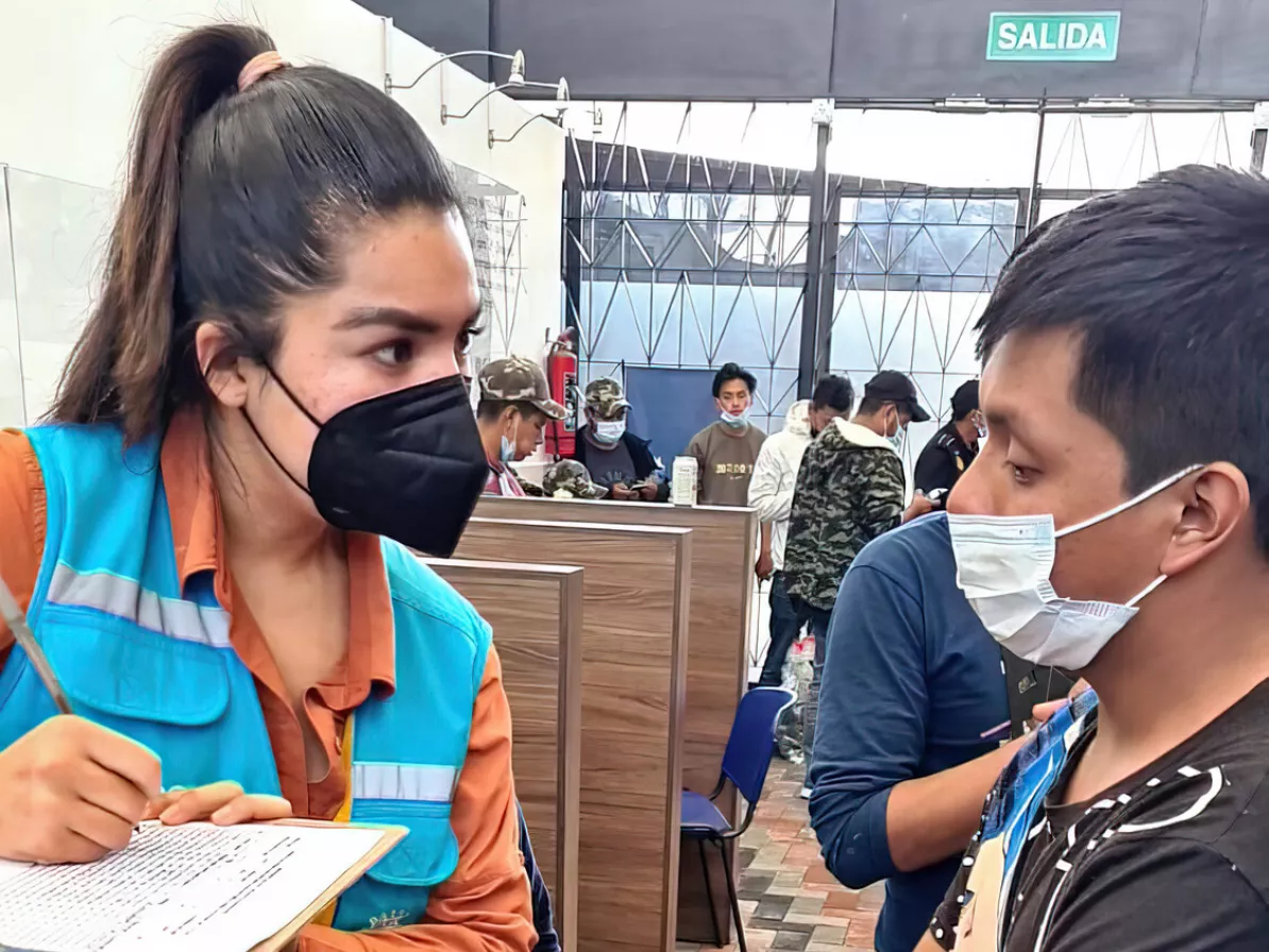 A young woman writing on a clip board talking to a young man