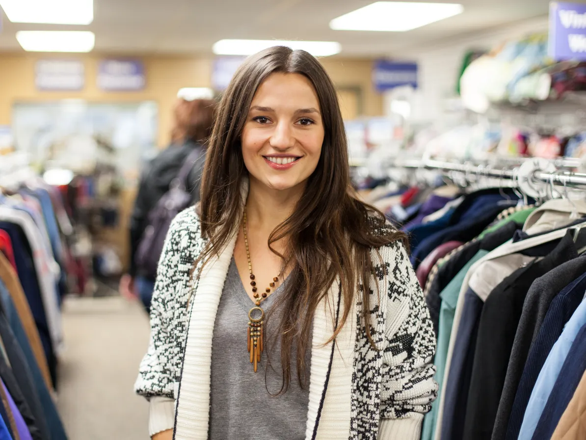 A thrift volunteer smiling with thrift store clothing racks in background