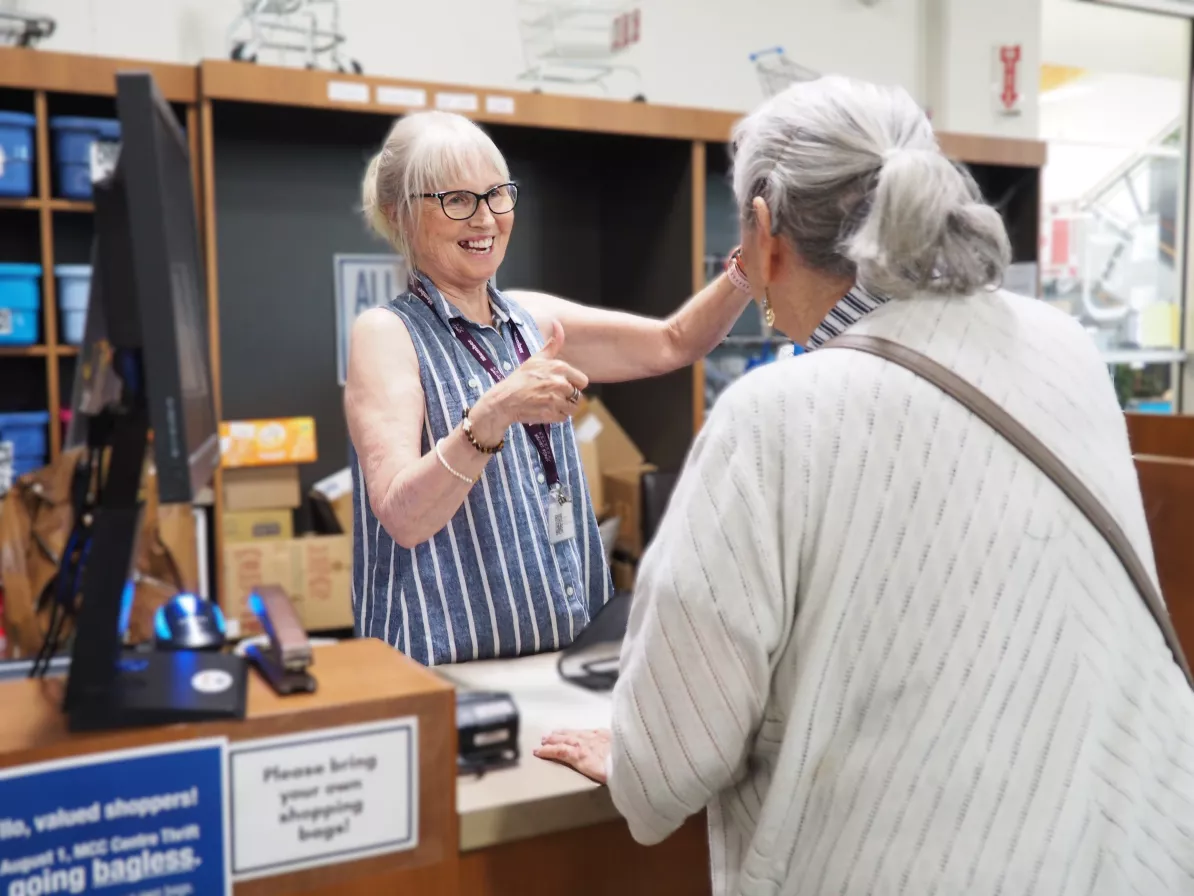 A volunteer cashier smiling as she opens a bag for a thrift shop customer