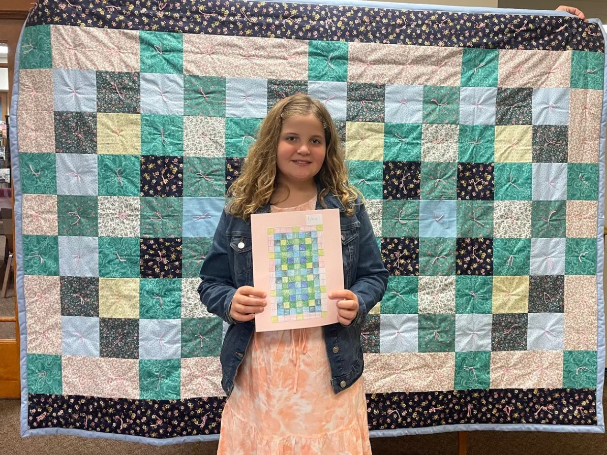 Nora Sandberg stands in front of the comforter she designed while holding the design grid.
