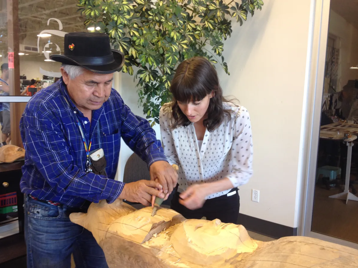 Isadore helping MCC intern Kaitlin with an Indigenous carving