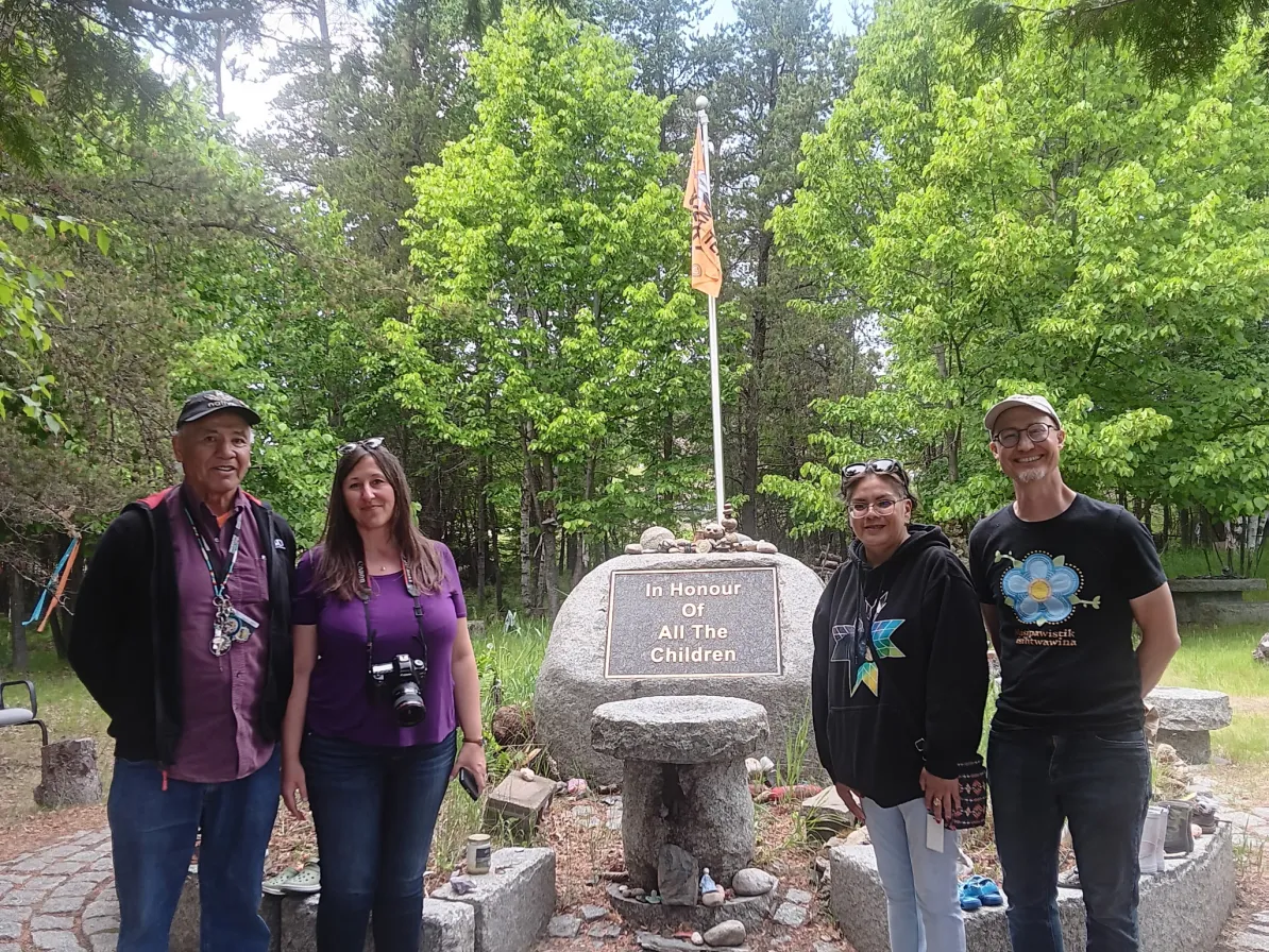 Four people stand beside the dedication plaque at Anamiewigummig (Kenora Fellowship Centre)