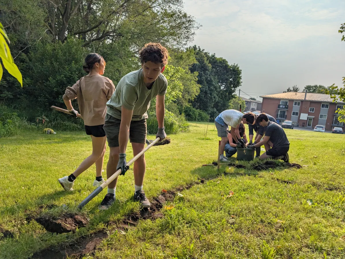 Two teenagers dig a path on a residential green space while other teens are in the background.