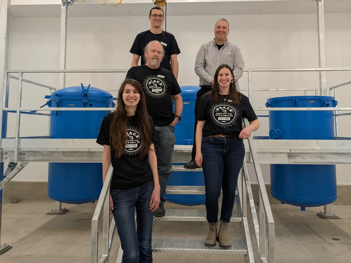 The Material Resource team wear black shirts (one does not) standing on stairs in the MCC cannery.