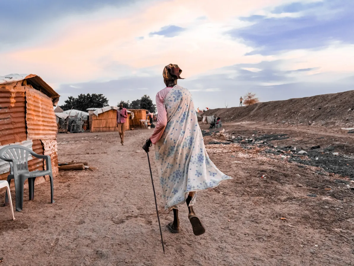 Mary Nyashin Tsief (70) leads MCC visitors to her home in Rubkona camp for people displaced by flooding and violent conflict. She has been living in the camp for four years She is a beneficiary of an