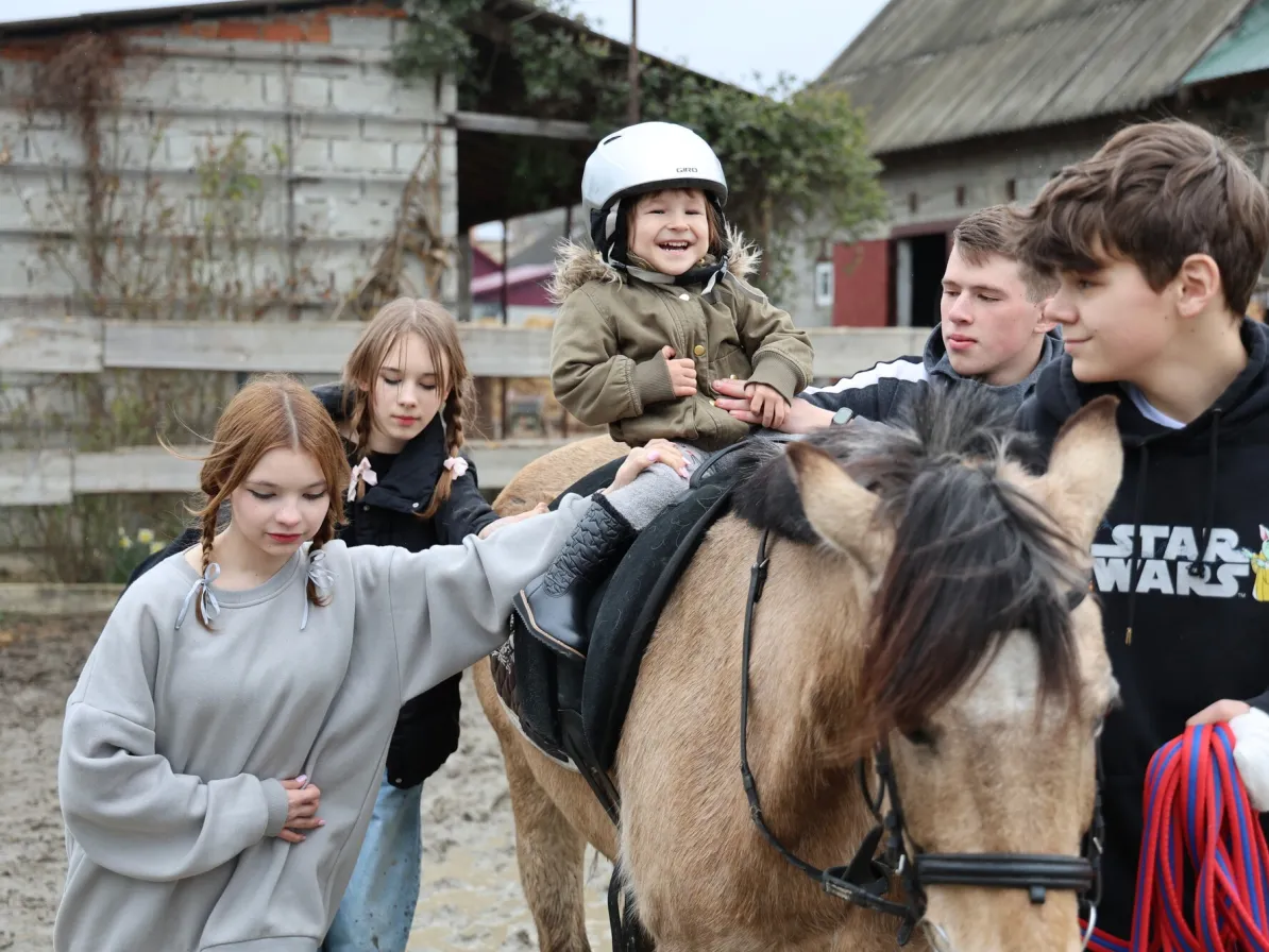 Three-year-old Vasylisa* sits calmly with assistance from volunteers during therapeutic horse riding for children who are displaced and affected by war.MCC, with partner Association of Mennonite B