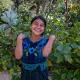 A young woman standing against a leafy background