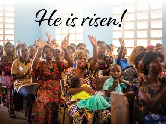 People in a church with hands raised and the words "He is risen!"