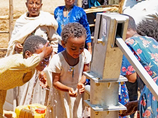 A group of children drinking from a well.