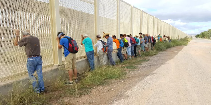 A group of people praying against a border wall
