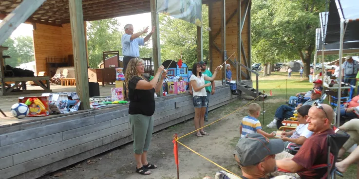 An auctioneer stands on an outdoor stage. Two women are down below displaying toys that are for auction.